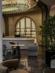 A modern bar seating area with concrete flooring and seating, featuring a well-stocked bar and comfortable chairs.