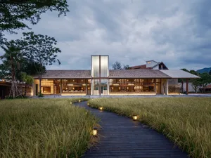 A modern building with wooden exterior and lighting along a pathway surrounded by grass.