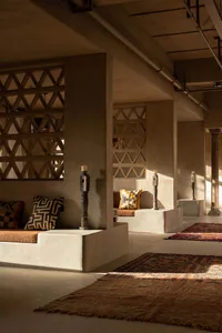 A spacious and modern lobby with concrete seating areas, patterned cushions, and wooden candle holders.