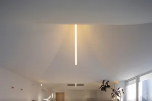 A modern room with a linear light fixture hanging from the ceiling, casting warm, indirect light.