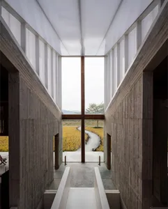 Modern lobby with concrete walls, glass windows, and a pathway leading to a natural landscape.
