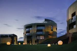 A modern building with a metal-clad exterior illuminated at dusk with spherical light installations in the foreground.