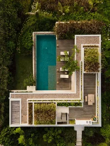 A modern minimalist residential exterior featuring a pool, wooden deck, gravel pathway, and lush greenery.
