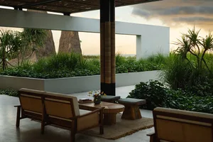 Modern patio area with wooden furniture, concrete floor, and tropical greenery in the background.