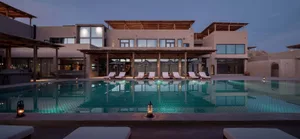 Modern pool house exterior with concrete walls and a serene pool area at dusk.