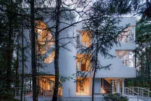 Modern residential building with large glass windows, white exterior, and stone base.