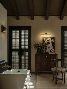 A modern residential bathroom featuring wooden elements and a freestanding bathtub with a brass faucet.