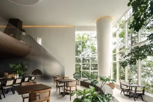 A stylish modern restaurant interior with concrete walls, wooden tables, and large windows overlooking greenery.