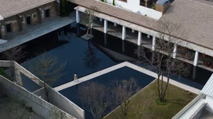 An aerial view of a modern swimming pool with a concrete floor and a clear pool filled with water, surrounded by buildings.