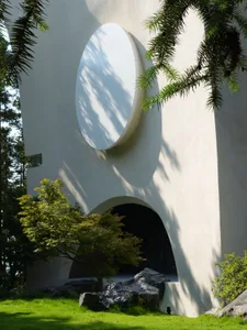 一棟現代白色水泥住宅，設有圓形窗戶，旁有樹枝。