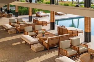 Outdoor lounge area with wooden furniture and a concrete floor near a poolside.