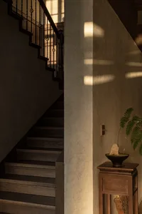 A staircase with concrete and wooden steps, illuminated by soft, natural light coming through a window.