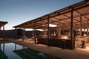Outdoor pool deck featuring a wooden pergola-covered bar with concrete countertop and seating areas.