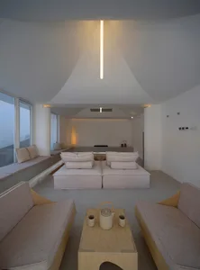 Minimalist living room with concrete walls, floor, and furniture. Light wooden coffee table with teapot and cups.