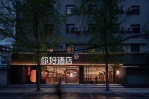The storefront of a hotel featuring glass walls, concrete elements, and illuminated lighting fixtures at dusk.