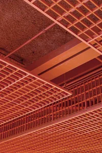 A close-up view of an industrial building interior featuring a steel grid structure and a textured, rusted ceiling.