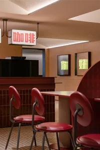 Industrial-style restaurant interior with tile and concrete counter, featuring red stools and a sign with Chinese characters.