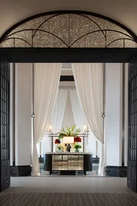 A luxury lobby featuring elegant white curtains with a decorative archway above the entrance, a table displaying flowers and 