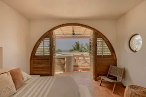 Bedroom with wooden doors and tile floor, featuring a bed with striped bedding and a wicker chair