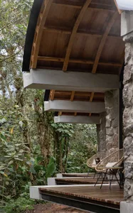 A minimalist outdoor seating area with wooden chairs, concrete steps, and stone walls amidst a lush green forest.