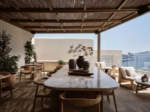 A minimalistic outdoor patio with wooden furniture and stone table, overlooking the ocean and a cruise ship.