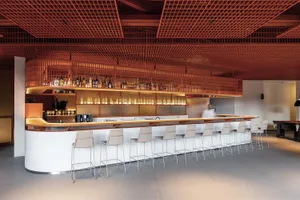 A modern bar with a wooden honeycomb grid ceiling and white stools.