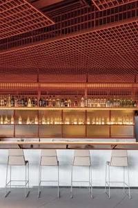 A modern bar interior featuring bar stools, metal ceiling, and a variety of bottles on shelves.