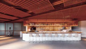 A minimalist bar counter with metal stools and a metal ceiling grid