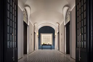 A modern hotel corridor with tiled flooring and patterned wallpaper and ceiling accents, featuring a central desk with a lamp