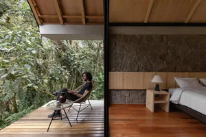 A modern minimalist bedroom featuring a wooden floor, stone wall, and simple furniture.