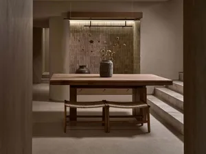 A minimalist dining room with a wooden table, chairs, and a vase of dried flowers.