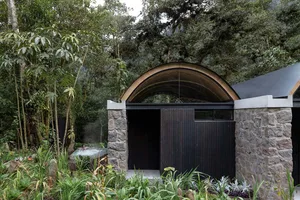 A modern minimalist spa hotel entrance featuring stone and wooden elements surrounded by lush greenery.