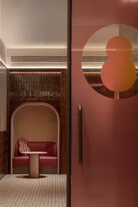 A modern red restaurant booth with a textured tile backdrop and a small round table with a red leather cushion and patterned 