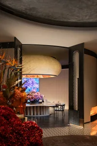 A modern restaurant interior featuring wood tables, fabric seating, and glass installations