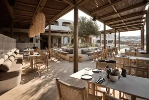 Outdoor restaurant setting with wooden tables, concrete flooring, and wicker chairs.