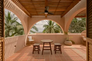 Vacation home veranda with wooden pergola, terracotta tiles, and tropical foliage.