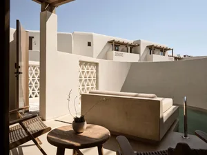 A modern vacation home with a concrete exterior and wooden accents, featuring a private pool and outdoor seating area.