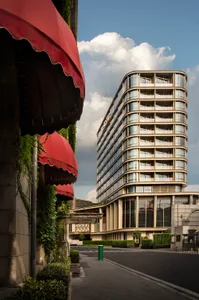 Outdoors shot of modern hotel with curved glass architecture, balconies, and lush greenery.