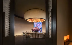 現代餐廳室內擺設木質家具，吊頂懸掛大型圓形燈具，並可見活動百葉簾。