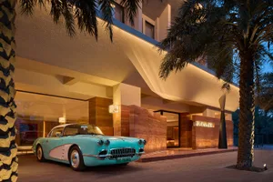 A classic blue and white car parked in front of a luxurious hotel entrance with concrete and marble finishes.