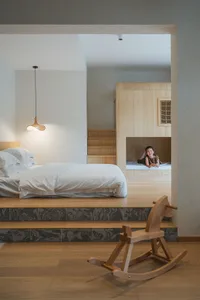 A minimalist family room featuring wood and marble materials, with a child sitting on a lower platform bed.