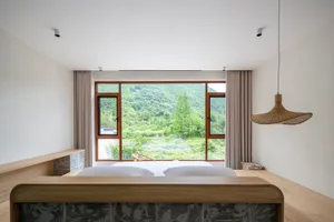 Modern bedroom with a wooden bed frame, ceramic tiles, and metal accents, featuring a view of a lush green landscape through 