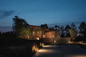 A modern building with wooden exterior and illuminated lights against a twilight sky.