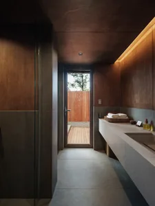 The image shows a minimalist bathroom featuring wooden walls and grey concrete flooring.