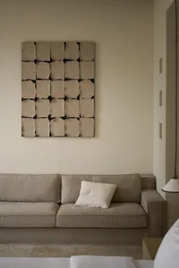 Modern, minimalist living room featuring a beige sofa with a textured fabric and a wall art piece composed of textured paper 