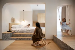 A modern playroom with warm tones, wooden and marble surfaces, and children playing on a wooden rocking horse and a swing.