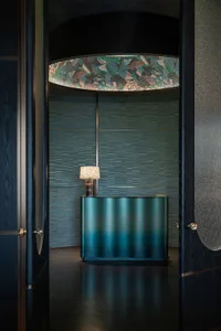 Modern reception desk with metallic finish, featuring a lamp and a patterned ceiling light.