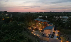 A modern residential house with stone walls and wooden accents, surrounded by trees at sunset.