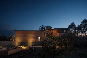 A modern house with wooden exterior at dusk, illuminated by warm lighting.