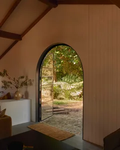 Interior view of a minimalist house featuring a wooden archway leading to a garden with greenery and plants.